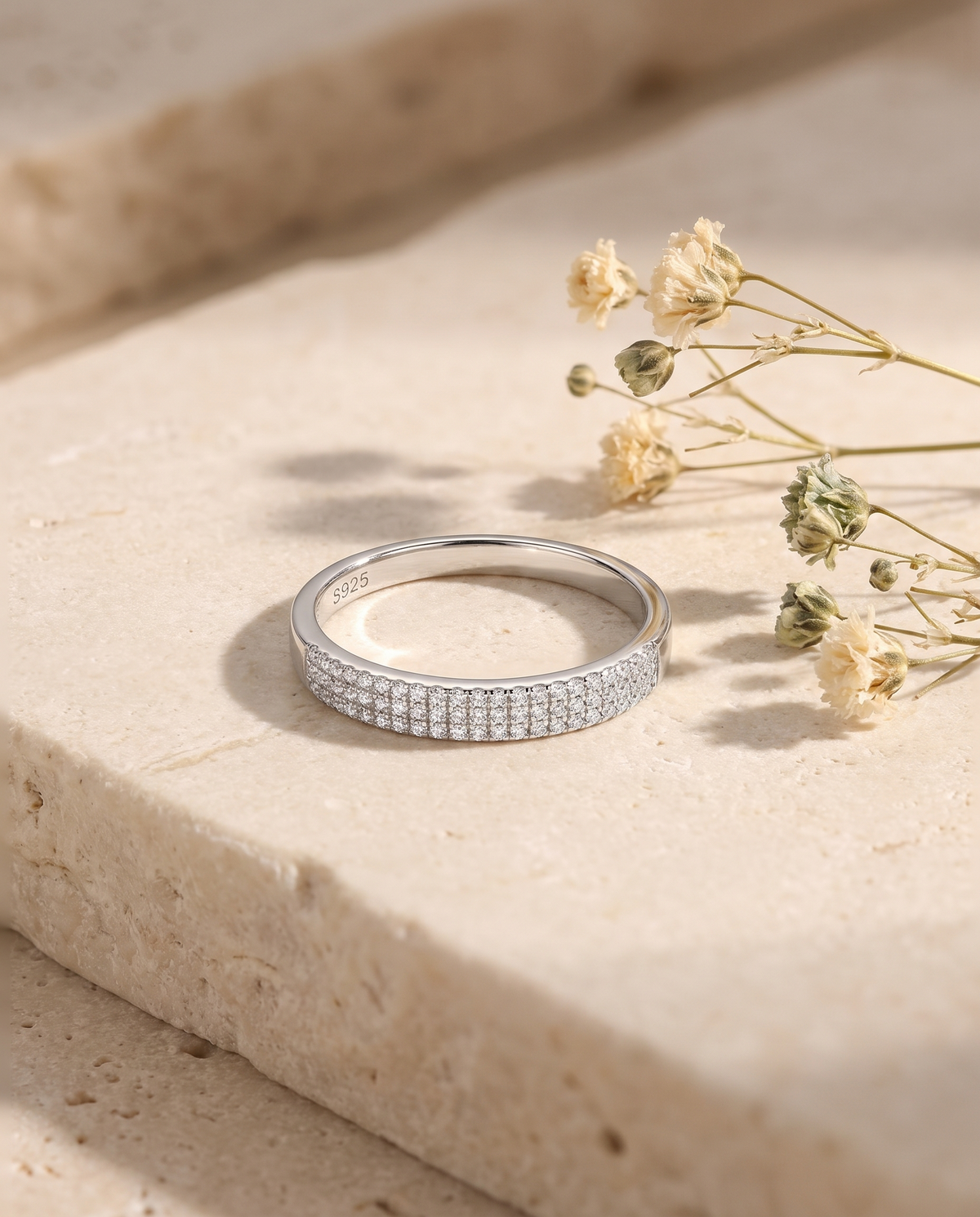 Silver moissanite pave band ring on pale limestone with dried flowers