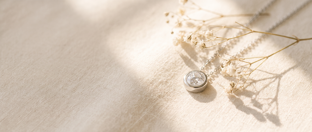 Moissanite pendant necklace on warm cream linen with dried gypsophila in morning sunlight